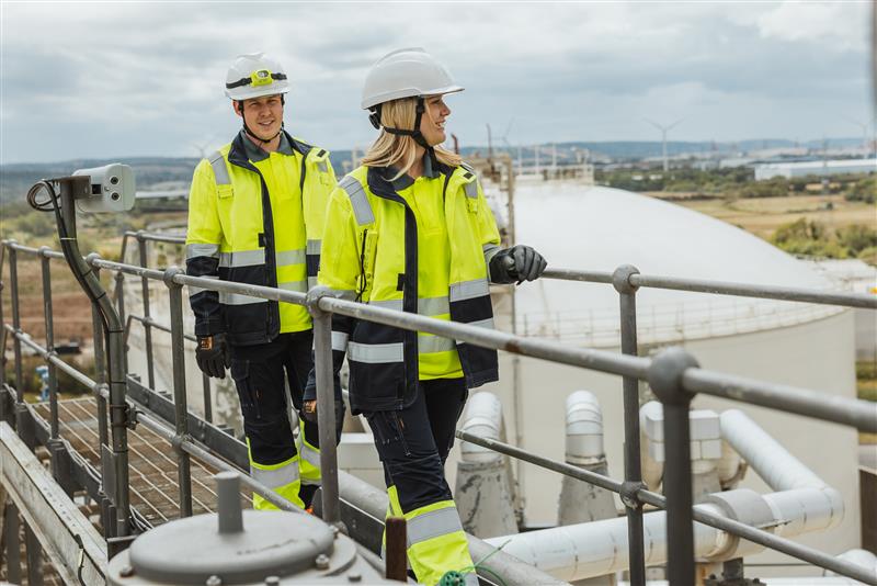 Two workers in high-visibility safety gear walking on an industrial platform